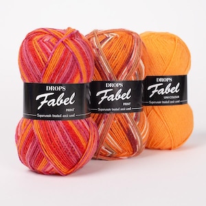 May include: Three skeins of Drops Fabel superwash treated sock wool yarn. The first is a variegated mix of pink, orange, and red. The second is a variegated blend of orange, brown, and white. The third is a solid bright orange color.