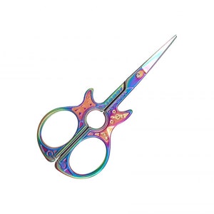 May include: Iridescent scissors with a guitar-shaped handle. The scissors have a rainbow finish with shades of purple, blue, green, and gold. The blades are sharp and pointed, and the handle has decorative floral details.