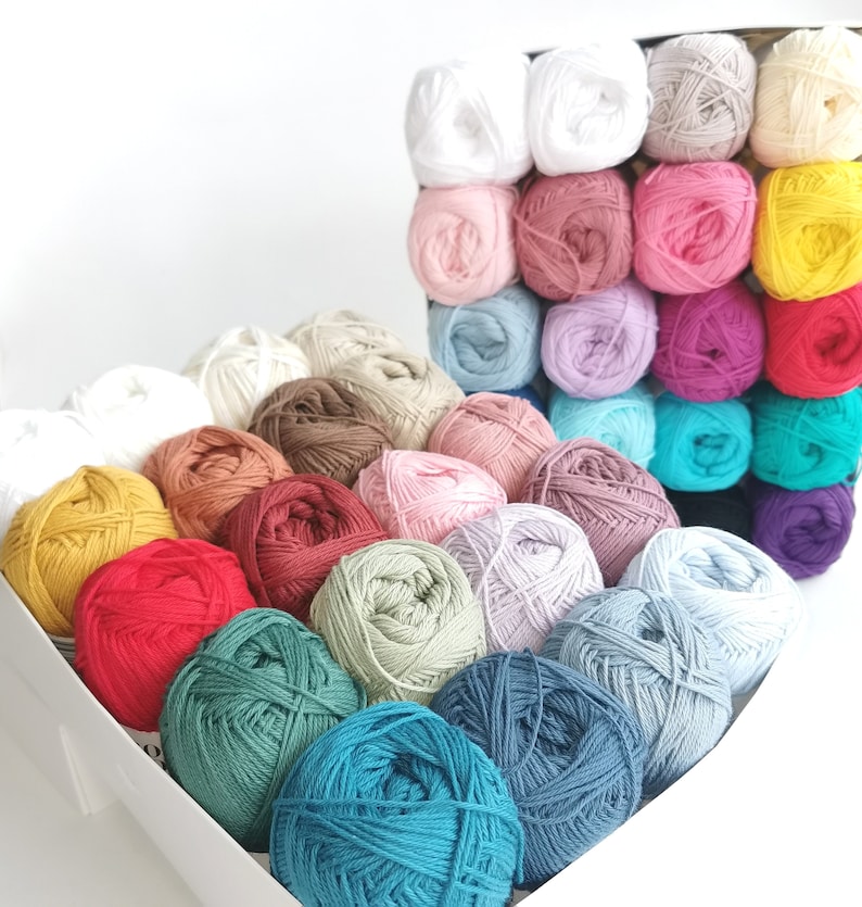 Puede incluir: Una colecci&oacute;n de ovillos de lana coloridos en una caja blanca. La lana est&aacute; dispuesta en filas e incluye tonos de blanco, rosa, rojo, amarillo, verde, azul y marr&oacute;n. Los ovillos est&aacute;n bien enrollados.