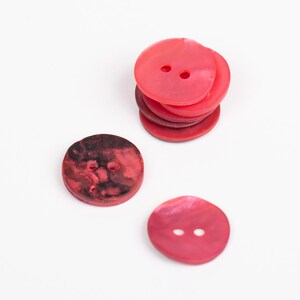 May include: A stack of four red shell buttons and two individual red shell buttons with two holes each.