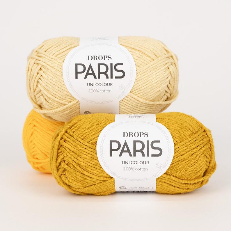 May include: Two skeins of Drops Paris Uni Colour 100% cotton yarn in shades of yellow. One is a light yellow, the other a mustard yellow. The yarn labels are white with black text.