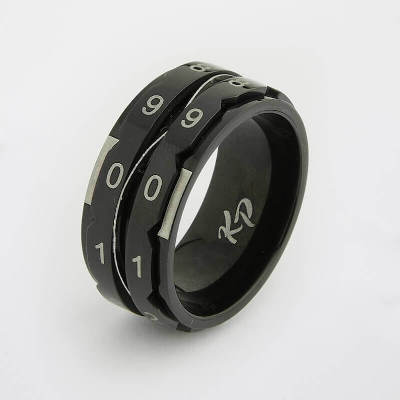 May include: Black spinning ring with three rotating bands, each with numbers 0, 1, and 9 engraved in silver. The ring has a black band with the letters "KZ" engraved in silver.