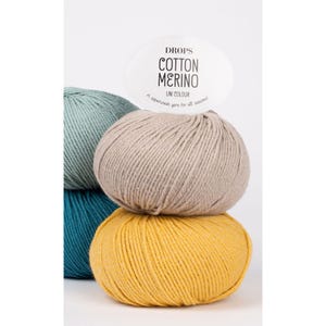 Puede incluir: Una pila de cuatro ovillos de lana Drops Cotton Merino en colores verde azulado, azul claro, beige y amarillo. El ovillo superior tiene una etiqueta ovalada blanca con el texto DROPS COTTON MERINO UNI COLOUR A superwash yarn for all seasons.