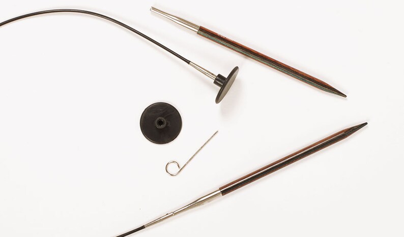 Puede incluir: Agujas de tejer y accesorios sobre un fondo blanco. El conjunto incluye dos agujas de tejer de madera con puntas met&aacute;licas, un cable negro, un tope negro y una peque&ntilde;a herramienta met&aacute;lica. Las agujas tienen un acabado marr&oacute;n oscuro.