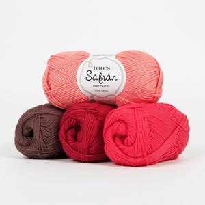 May include: A collection of five yarn balls in shades of pink, red, and brown. The top ball is a light coral color, with a label that reads "Drops Safran Uni Colour 100% cotton." The other balls are various shades of red and brown.