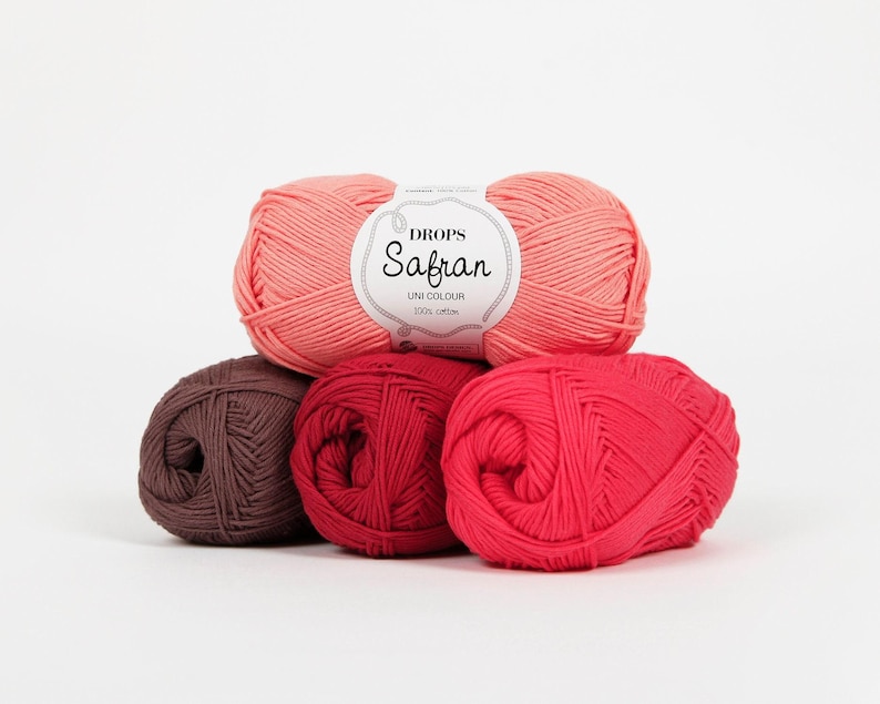 May include: A collection of five yarn balls in shades of pink, red, and brown. The top ball is a light coral color, with a label that reads "Drops Safran Uni Colour 100% cotton." The other balls are various shades of red and brown.