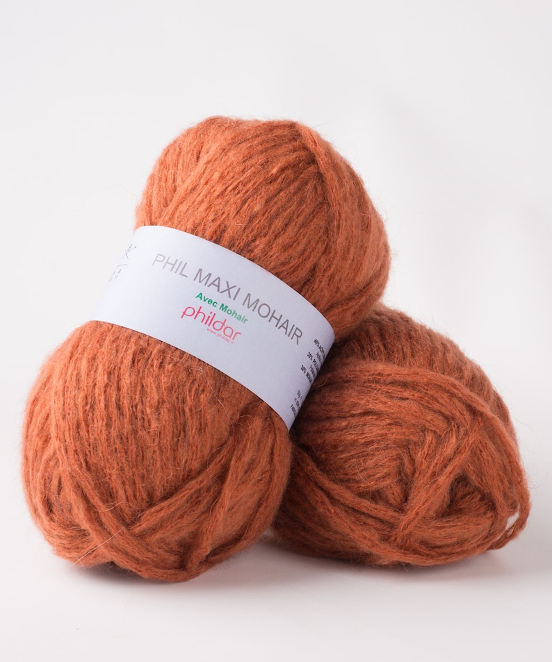 May include: Two balls of orange-brown yarn, labeled "PHIL MAXI MOHAIR" with "Avec Mohair" and the brand name "phildar" on a white label. The yarn has a fluffy texture, suitable for knitting or crochet projects.