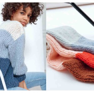 May include: A woman wearing a color-blocked sweater in shades of white, light blue, and navy blue. Beside the woman are several knitted arm warmers in various colors, including pink, gray, brown, and orange. The items appear to be handmade.