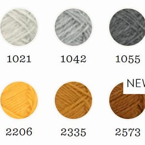 May include: A collection of ten circular yarn samples arranged in two rows, featuring colors ranging from cream, light gray, and charcoal to black, yellow, mustard, and brown. Each sample is labeled with a numerical code, and one is marked NEW.