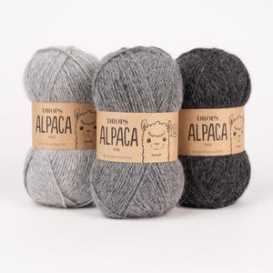 May include: Three skeins of yarn in varying shades of gray, ranging from light to dark charcoal. Each skein is wrapped in a tan paper band featuring the text DROPS ALPACA MIX and a line drawing of an alpaca face on the front of the label.