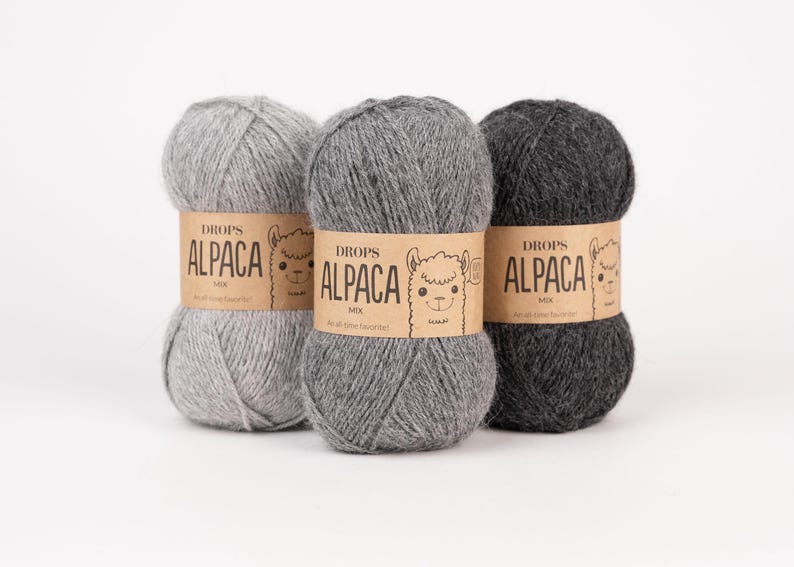 May include: Three skeins of yarn in varying shades of gray, ranging from light to dark charcoal. Each skein is wrapped in a tan paper band featuring the text DROPS ALPACA MIX and a line drawing of an alpaca face on the front of the label.