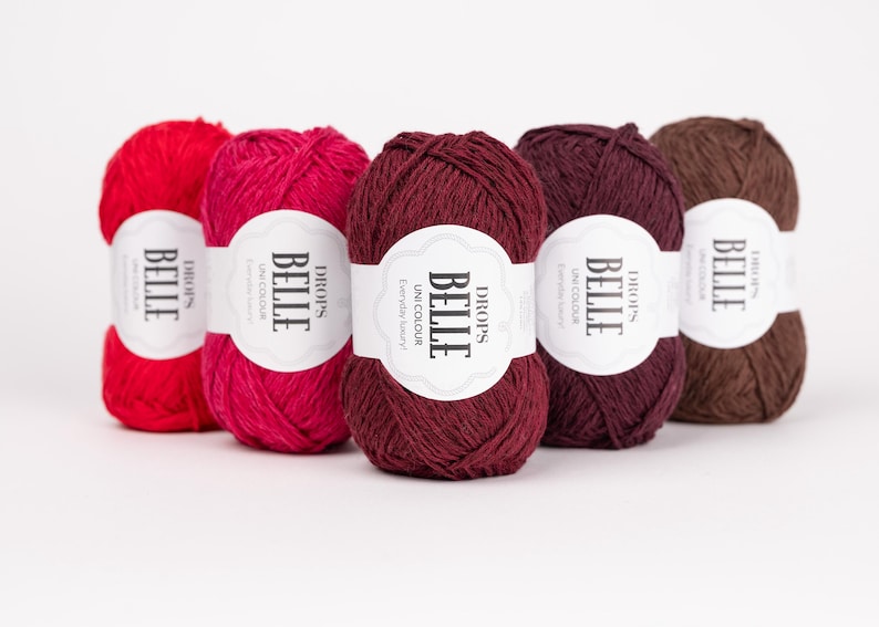 May include: Five skeins of Drops Belle yarn in various colors: red, fuchsia, burgundy, dark purple, and brown. Each skein has a white label with the text "BELLE" and "UNI COLOUR". The yarn is for knitting and crochet projects.