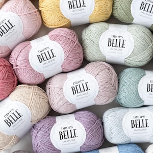 May include: A collection of Drops Belle yarn in various pastel colors, including pink, yellow, and blue. Each skein has a label that reads "Drops Belle Uni Colour Everyday luxury!"