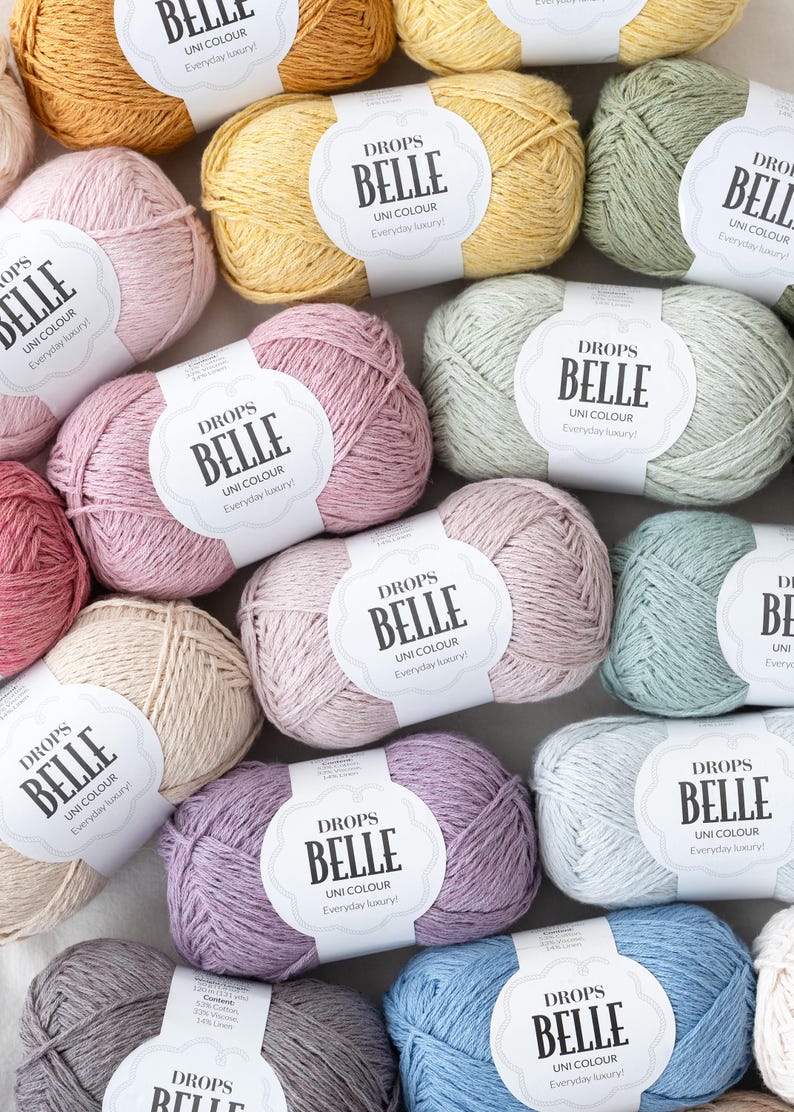 May include: A collection of Drops Belle yarn in various pastel colors, including pink, yellow, and blue. Each skein has a label that reads "Drops Belle Uni Colour Everyday luxury!"