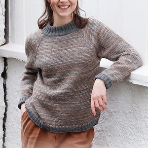 May include: A long-sleeved knit sweater featuring a heathered brown, gray, and orange horizontal striped pattern. The garment has a solid dark gray ribbed crew neckline, matching ribbed cuffs, and a ribbed hemline with raglan sleeve detailing.