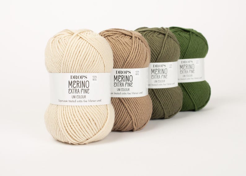 May include: Four balls of Drops Merino Extra Fine Uni Colour yarn in cream, tan, olive green, and dark green. Each ball has a white label with black text. The yarn is tightly wound, showing the texture of the merino wool.