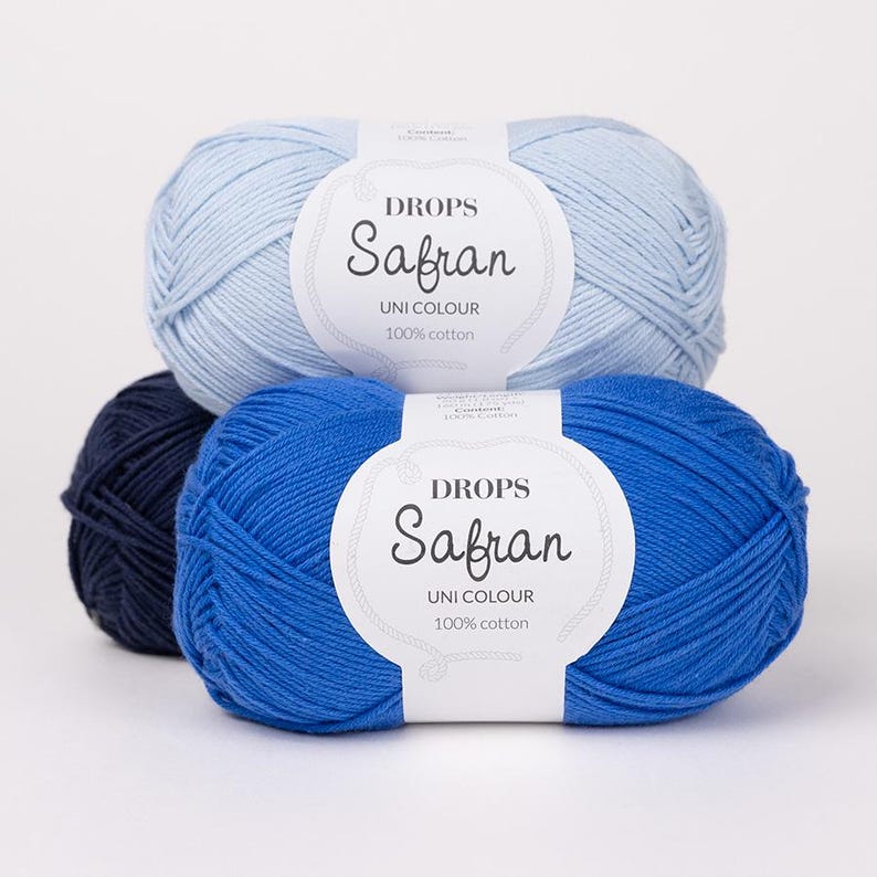 May include: Three balls of Drops Safran Uni Colour 100% cotton yarn in shades of blue. The top ball is light blue, the middle is a vibrant blue, and the bottom left is a dark navy blue. Each ball has a white label with the brand name.