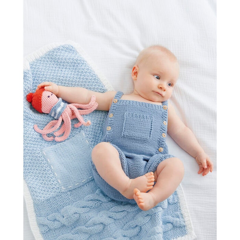 Puede incluir: Un beb&eacute; con un mono de punto azul claro con botones y un bolsillo. El beb&eacute; est&aacute; tumbado en una manta de punto azul con un borde blanco. El beb&eacute; est&aacute; sosteniendo un juguete de punto de pulpo rosa y rojo.