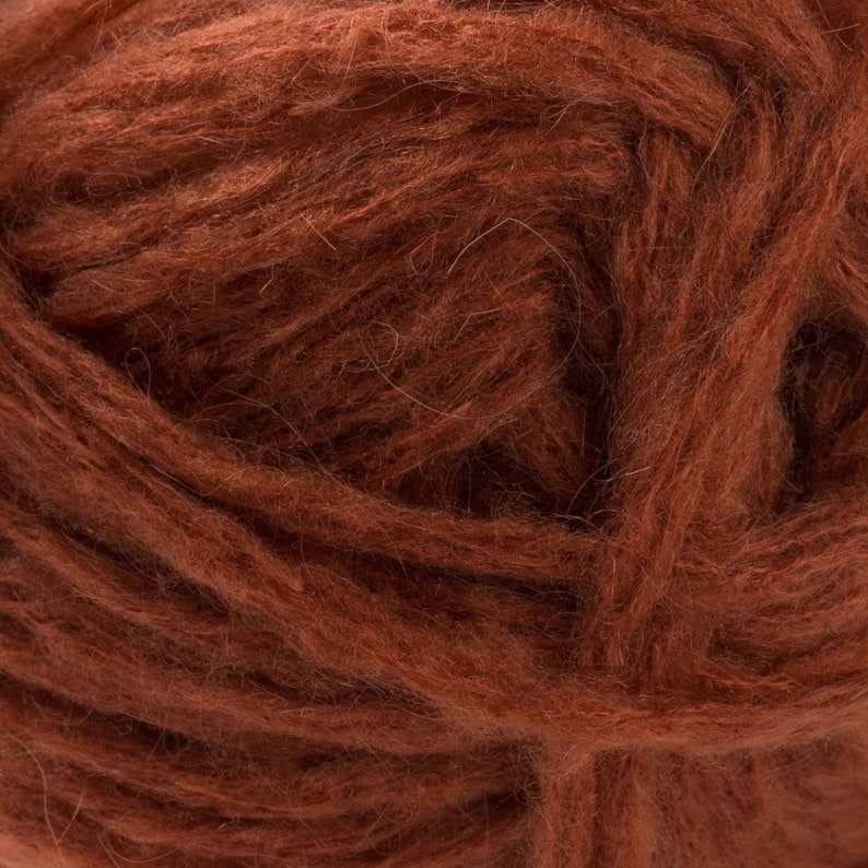 May include: Close-up of a ball of brown yarn. The yarn has a fluffy, textured appearance, with visible strands and a rich, earthy color. The fibers are tightly wound, creating a dense, soft ball, suitable for knitting or crocheting projects.