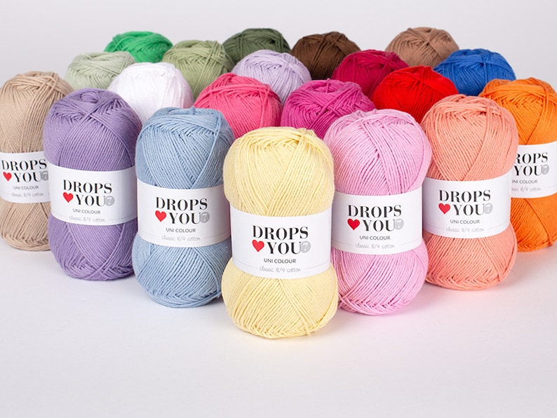 Puede incluir: Una colecci&oacute;n de ovillos de lana coloridos en varios tonos, incluyendo lavanda, azul, rosa y naranja. Cada ovillo tiene una etiqueta blanca con el texto "DROPS YOU" y "UNI COLOUR". La lana est&aacute; dispuesta de forma visualmente atractiva.