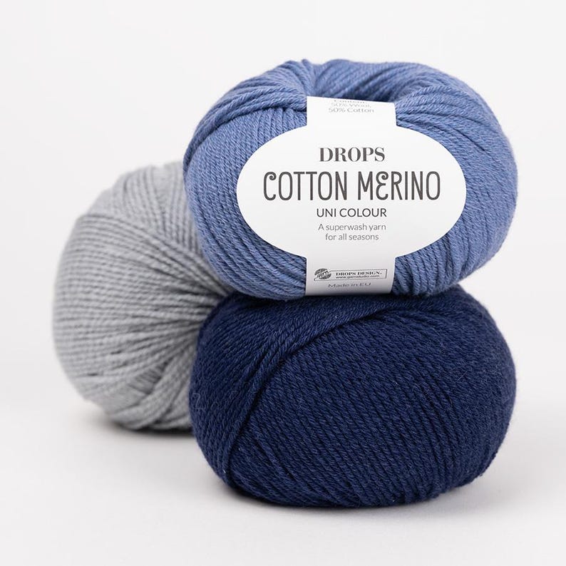 Puede incluir: Tres ovillos de lana Drops Cotton Merino en gris claro, azul medio y azul marino oscuro. El ovillo azul tiene una etiqueta de papel blanco con el texto Drops Cotton Merino, Uni Colour, A superwash yarn for all seasons y Made in EU.