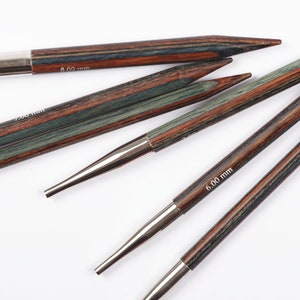 Puede incluir: Un conjunto de agujas de tejer de madera con puntas met&aacute;licas. Las agujas presentan un dise&ntilde;o a rayas en tonos marr&oacute;n, verde y rojo. Las tallas est&aacute;n marcadas como 6,00 mm y 8,00 mm.