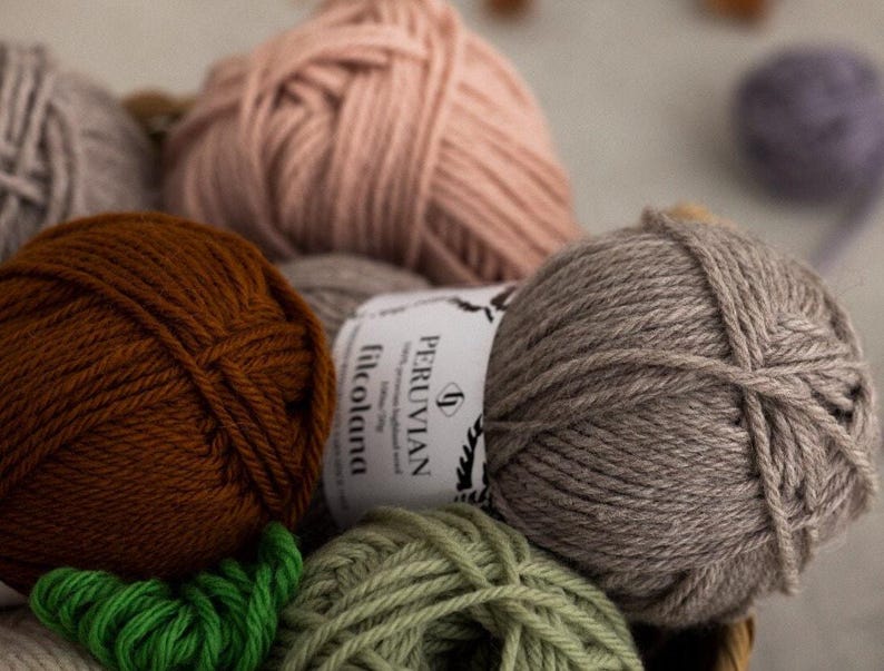 May include: A close-up of four balls of yarn in various colors: brown, gray, pink, and green. The yarn is labeled 'PERUVIAN filcolana'.