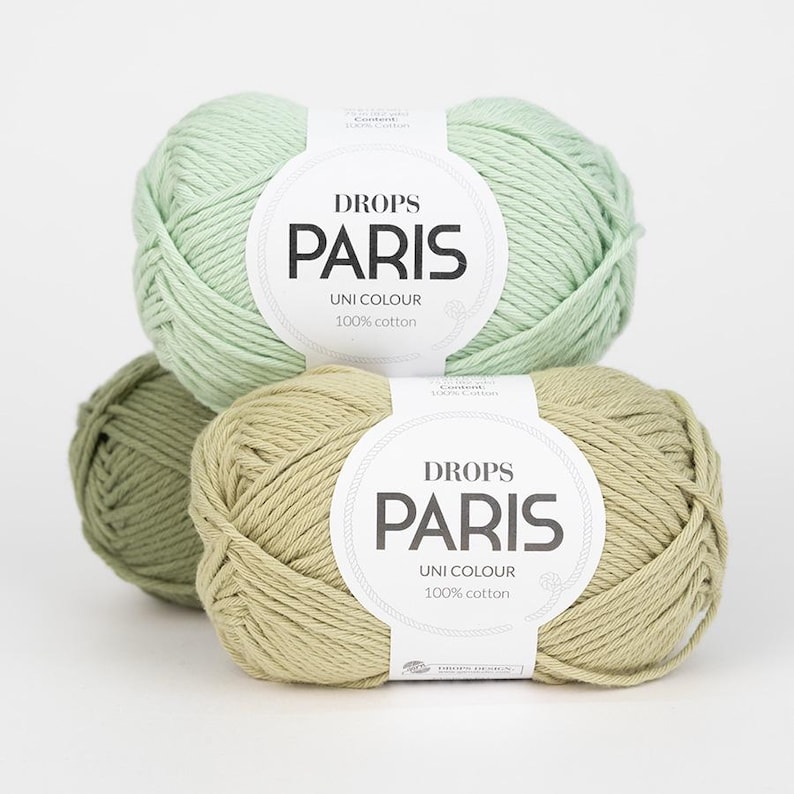 K&ouml;nnte beinhalten: Drei Kn&auml;uel Drops Paris Uni Colour 100% Baumwollgarn in Gr&uuml;n- und Beiget&ouml;nen. Das Garn ist fest zu Kugeln gewickelt, mit Etiketten, die den Markennamen und Produktdetails zeigen. Ideal f&uuml;r Strick- und H&auml;kelprojekte.