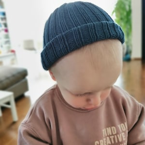 Puede incluir: Un ni&ntilde;o con una boina de punto azul oscuro y una sudadera marr&oacute;n claro con el texto "Find You Creative" impreso.