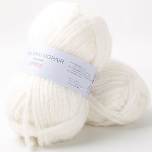 May include: Two fluffy white yarn balls of Phil Maxi Mohair. The yarn has a soft, textured appearance. A label wrapped around the yarn ball displays the brand name and fiber composition: 40% Acrylic, 30% Polyamide, and 30% Mohair.