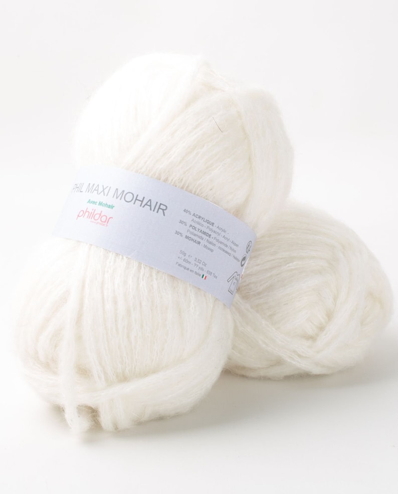 May include: Two fluffy white yarn balls of Phil Maxi Mohair. The yarn has a soft, textured appearance. A label wrapped around the yarn ball displays the brand name and fiber composition: 40% Acrylic, 30% Polyamide, and 30% Mohair.