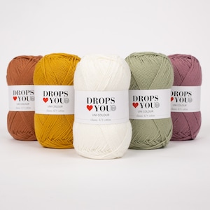Puede incluir: Cinco ovillos de hilo Drops You Uni Colour en tonos &oacute;xido, amarillo mostaza, crema, verde salvia y malva. Cada ovillo tiene una etiqueta con el nombre de la marca y los detalles del producto. El hilo es algod&oacute;n cl&aacute;sico 8/4.