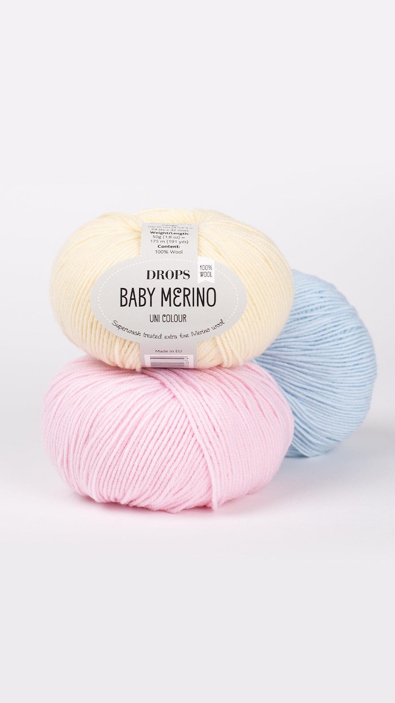 May include: Three balls of yarn in pink, light blue, and cream. The cream ball has a label that reads 'DROPS 100% WOOL BABY MERINO UNI COLOUR Superwash treated extra fine Merino wool Made in EU'.