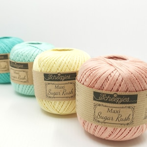 Puede incluir: Cuatro ovillos de lana en diferentes colores pastel: azul verdoso, verde claro, amarillo y melocot&oacute;n. Cada ovillo tiene una etiqueta marr&oacute;n con el texto "Scheepjes Maxi Sugar Rush" impreso en ella.