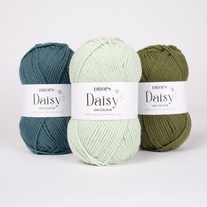 May include: Three skeins of Drops Daisy yarn in teal, light mint green, and olive green. Each skein features a white paper label with the text "DROPS Daisy UNI COLOUR 100% extra fine merino wool" printed in black, centered on the yarn.