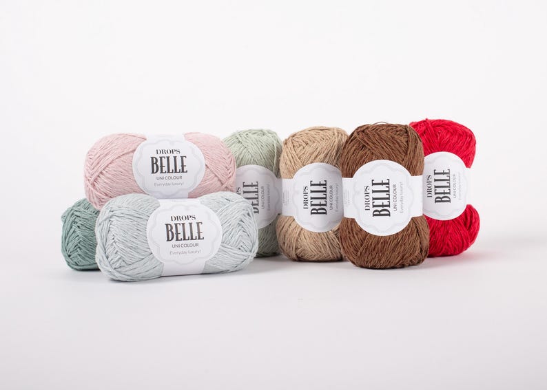 May include: A collection of colorful yarn skeins, including shades of pink, green, tan, brown, and red. Each skein has a white label with the text "BELLE" and "UNI COLOUR". The yarn is arranged on a white surface.