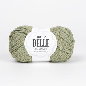 May include: A ball of sage green yarn with a white label that reads "DROPS BELLE UNI COLOUR Everyday luxury!" The yarn is tightly wound and appears soft. Ideal for knitting and crochet projects.