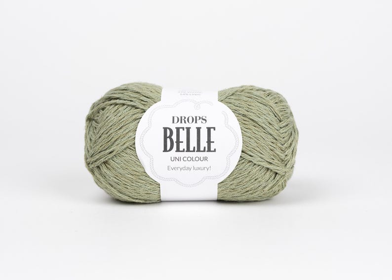May include: A ball of sage green yarn with a white label that reads "DROPS BELLE UNI COLOUR Everyday luxury!" The yarn is tightly wound and appears soft. Ideal for knitting and crochet projects.