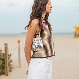 May include: A woman wearing a striped tank top and white denim shorts carries a silver bucket bag with a drawstring closure.