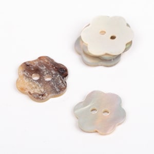 Può includere: Bottoni a forma di fiore in vari colori. Un bottone è marrone e beige, mentre altri sono bianchi e grigi iridescenti. Ogni bottone ha due fori per cucire. I bottoni sono fatti di un materiale lucido, forse simile a un guscio.