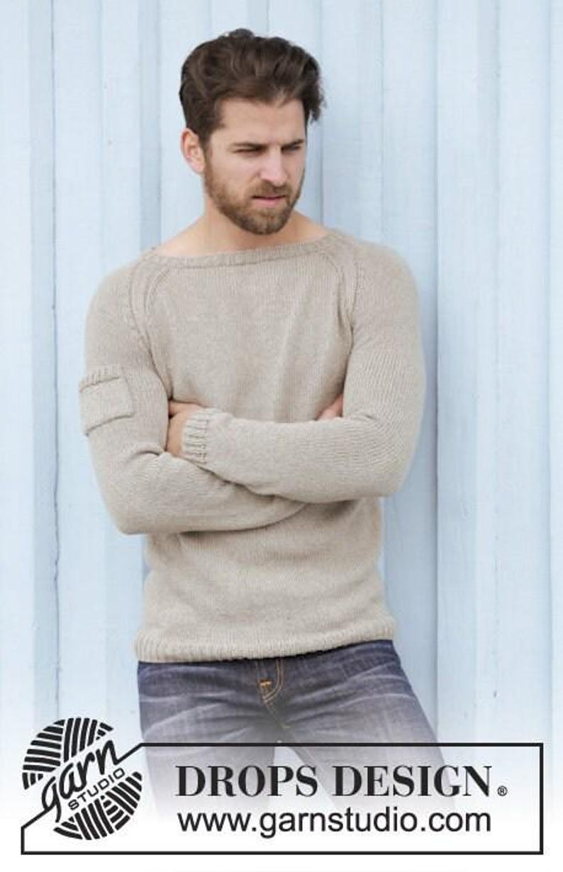 May include: A light beige sweater with a crew neck and a small pocket on the left sleeve. The sweater is paired with blue jeans. The image includes the text "DROPS DESIGN" and "www.garnstudio.com".