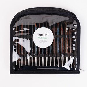 Puede incluir: Un estuche negro con cremallera y una parte delantera transparente que muestra un juego de agujas de tejer circulares intercambiables. Las agujas son de varios tonos de marr&oacute;n y plata, con tama&ntilde;os marcados en mil&iacute;metros. El estuche tiene una etiqueta blanca que dice "DROPS PRO Romance".