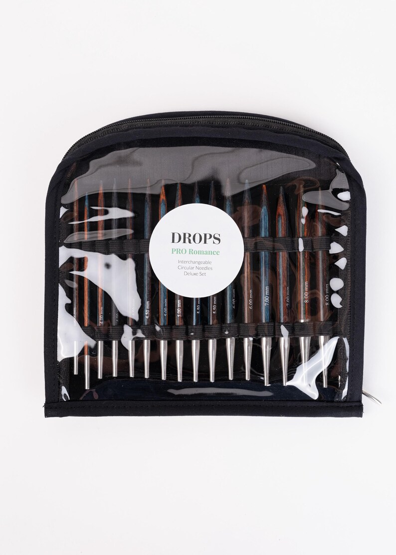 Puede incluir: Un estuche negro con cremallera y una parte delantera transparente que muestra un juego de agujas de tejer circulares intercambiables. Las agujas son de varios tonos de marr&oacute;n y plata, con tama&ntilde;os marcados en mil&iacute;metros. El estuche tiene una etiqueta blanca que dice "DROPS PRO Romance".