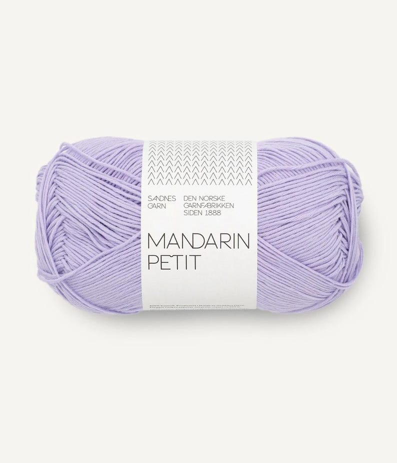 May include: A ball of lavender-coloured Mandarin Petit yarn. The yarn is wrapped with a white label that has the text "MANDARIN PETIT" and other text. The yarn is tightly wound and ready for knitting or crocheting projects.