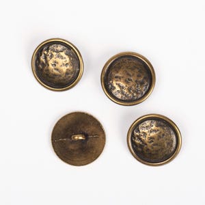 May include: Four antique gold-toned buttons with a textured surface. The buttons are round and have a raised rim.