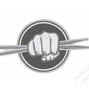 May include: A circular embroidered patch featuring a white clenched fist holding two crossed drumsticks against a dark gray background. The design is enclosed by a thick white border, and the text Embroidery Patterns appears in the bottom right.