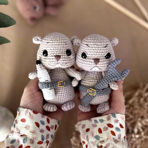 May include: Two crocheted animal dolls, each with a light beige body, black eyes, and a brown nose. One doll holds a white bottle, the other a blue wrench. Both wear a gray belt. The dolls are handmade.