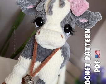 May include: A plush cow toy made of grey and cream yarn with a pink bow on its head, long eyelashes, and a brown yarn necklace featuring a small silver bell. The text CROCHET PATTERN PDF is visible on the right side next to a small American flag icon.