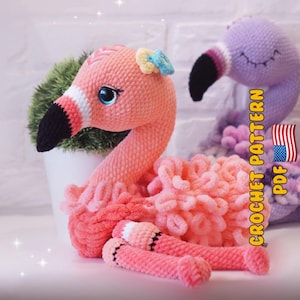 May include: A handmade pink crochet flamingo with a black beak, blue eyes, and a small flower on its head. The flamingo is lying down, with its legs extended. A second purple flamingo is in the background. The image includes the text "CROCHET PATTERN PDF".