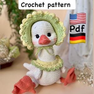 May include: A handmade crochet goose doll with a white body, a pink beak, and black eyes. The goose wears a green and yellow bonnet and collar. The image includes the text "Crochet pattern" and a PDF symbol with the American and German flags.
